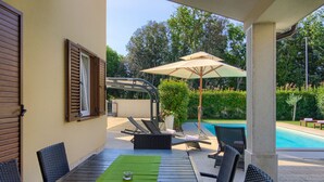 A covered outdoor seating area with a pool, lounge chairs, and a table with a green mat.
