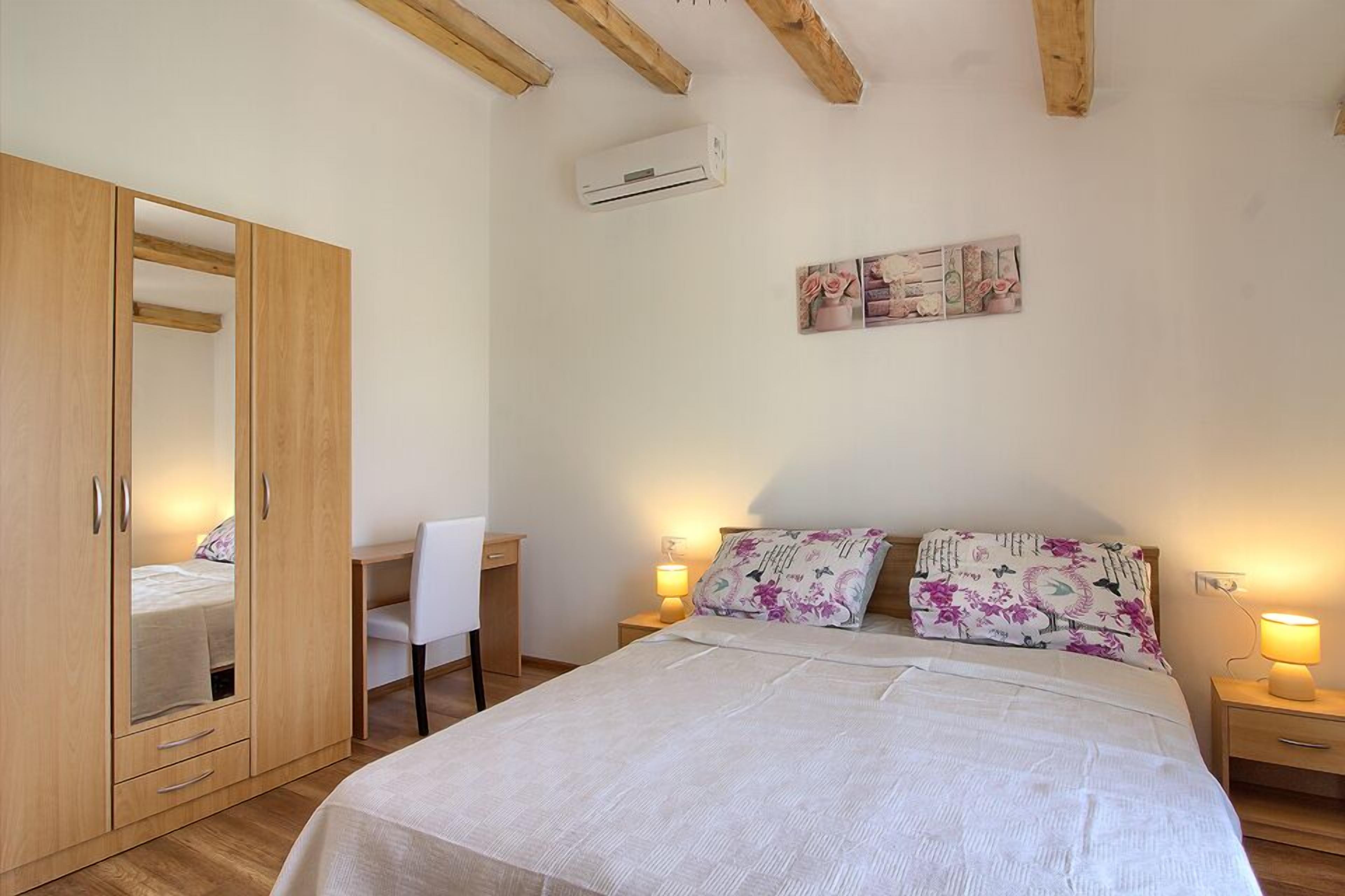 Un dormitorio con cama, escritorio, silla, armario y lámparas de noche.