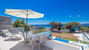 A terrace with a table, chairs, and an umbrella overlooking a pool and a scenic view of the sea. - Villa Punat seafront villa by Wiibuk (Kvarner - Punat) (Punat)