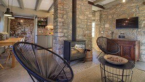A rustic interior with exposed stone walls, a wood-burning stove, a dining area with a wooden table and chairs, and a television mounted on the wall. - Villa KALU (Istria - Mrgani) (Mrgani)