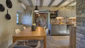 A dining area with a wooden table and chairs, a stone wall, and a kitchen with cabinets and a countertop. - Villa KALU (Istria - Mrgani) (Mrgani)