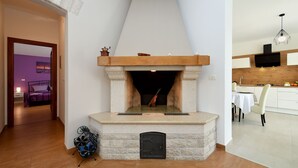 A modern living room with a stone fireplace, a dining area with a table and chairs, and a kitchen with a wooden countertop and a hanging light fixture. - Villa Natali (Istria - Galižana) (Galižana)