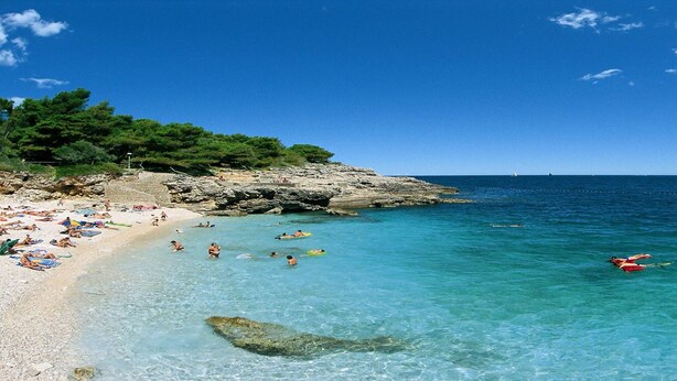 A beach with clear turquoise water, rocky cliffs, and a sandy shore.