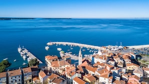 An aerial view of a coastal town with a marina, buildings with red-tiled roofs, and a prominent white church. - Villa Tartufo by WiiBuk (Istria - Svetvinčenat) (Svetvinčenat)