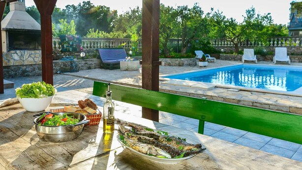 An outdoor dining area with a pool, a grill, and lounge chairs.