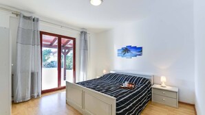 A bedroom with a bed, a nightstand, a lamp, and a view of the outdoors.