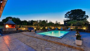 A stone-paved outdoor area with a swimming pool, lounge chairs, and a stone fireplace.