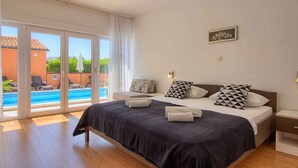 A bedroom with a large bed, a view of a swimming pool, and a balcony.