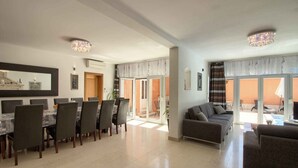 A spacious living area with a dining table and chairs, a sofa, and a chandelier.