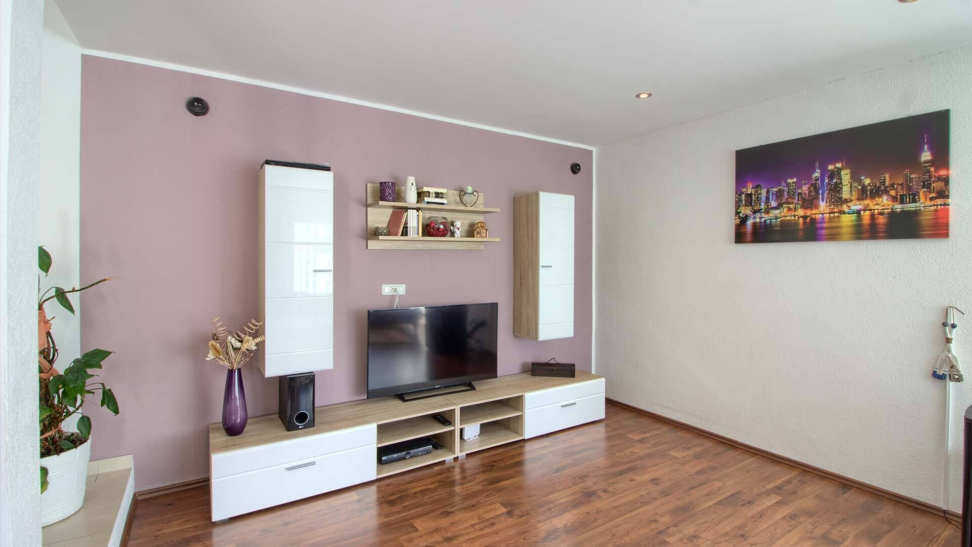 A modern living room with a flat-screen TV, wooden entertainment unit, and a cityscape painting.
