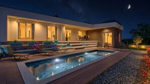 Et moderne hus med swimmingpool, udendørs siddepladser og en have.