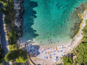 An aerial view of a beach with clear turquoise water, a sandy shore, and several beach umbrellas and sun loungers.