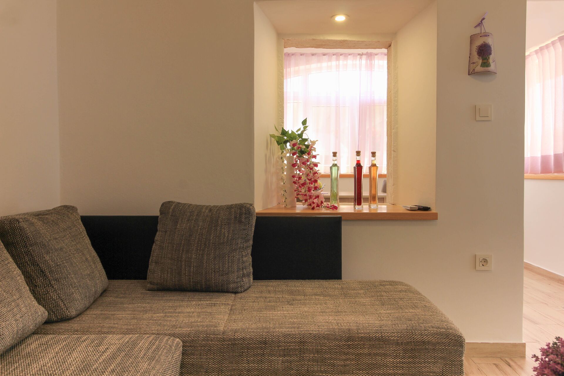 A living room with a sofa, a small table with decorative items, and a window with sheer curtains.