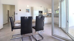 A modern kitchen with white cabinets, a microwave, and a stove. There is a dining area with a table and chairs.