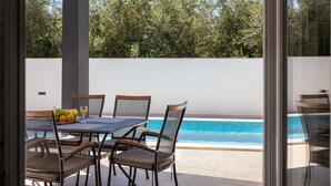 A patio with a table and chairs, a fruit bowl, and a view of a swimming pool.