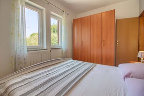 Quarto com uma cama, duas janelas, um radiador e um guarda-roupa.