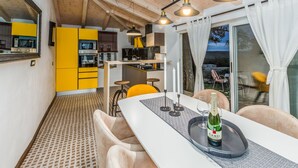 A modern kitchen with yellow cabinets, a dining area with a white table, and a view of the outdoors through large windows. - Villa NEVIA (Istria - Ripenda Verbanci) (Ripenda Verbanci)