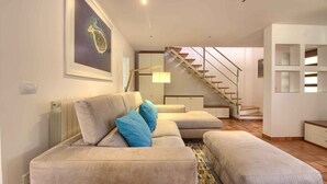 A modern living room with a beige sofa, blue cushions, a patterned rug, a staircase, and a minimalist shelving unit. - Villa Donatella (Istria - Sisan) (Sisan)