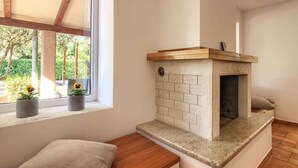 A corner room with a built-in fireplace, a window with potted plants, and a wooden bench. - Villa Donatella (Istria - Sisan) (Sisan)