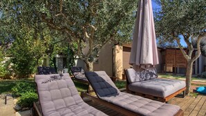 A deck with two lounge chairs and an umbrella, surrounded by olive trees and a building with a wooden facade. - Villa Donatella (Istria - Sisan) (Sisan)