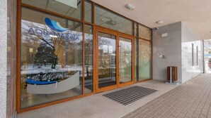 A modern building with large glass windows, a wooden door, and a tiled walkway. - Charming Studio with Balcony | Parking | Close to the Beach (Świnoujście)