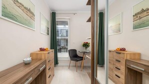 A narrow room with wooden cabinets, a chair, a small table, and artwork on the walls. - Charming Studio with Balcony | Parking | Close to the Beach (Świnoujście)