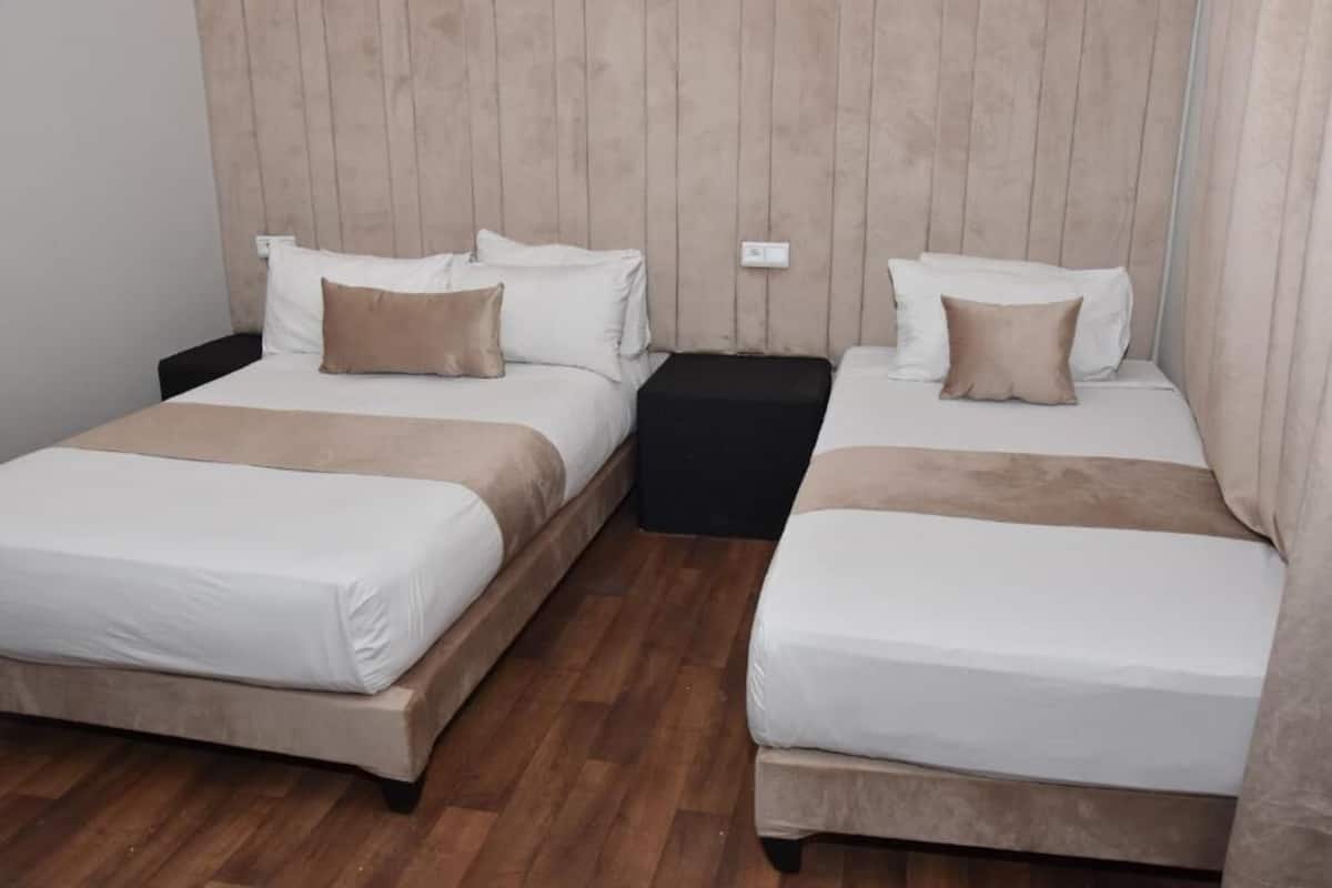 A hotel room with two beds, each with white bedding and a brown throw blanket. The room has a wooden headboard and a black nightstand between the beds.