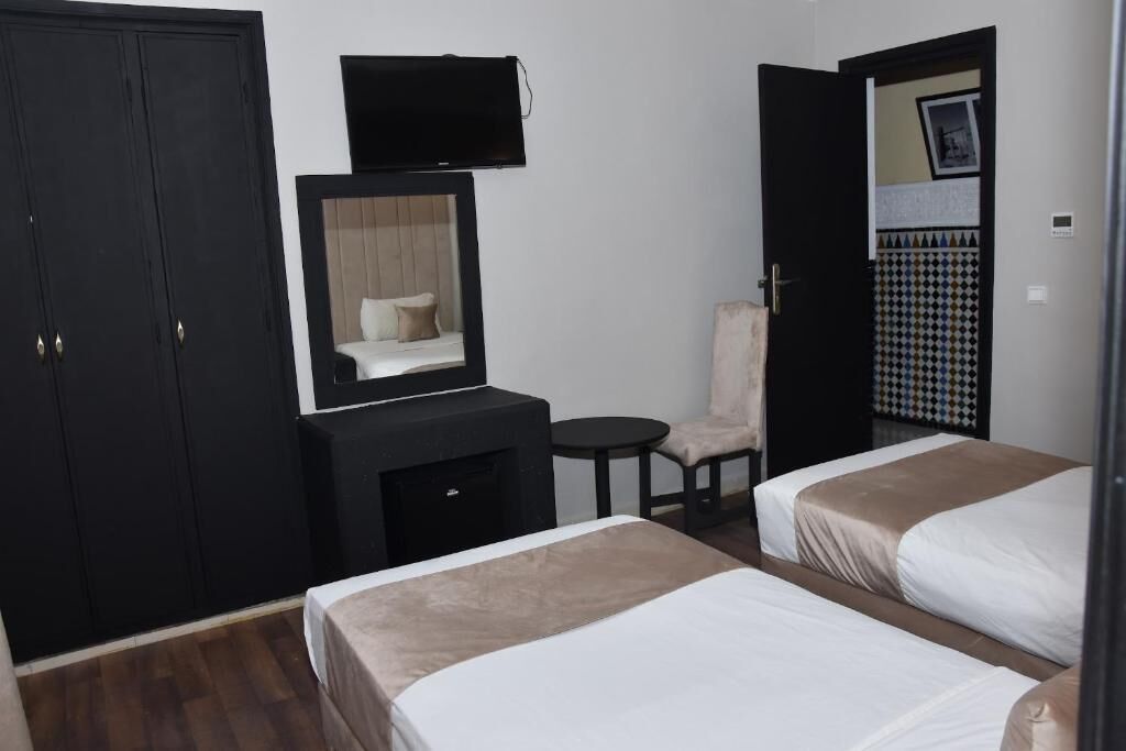 A hotel room with two beds, a TV mounted on the wall, a small table, and a chair.