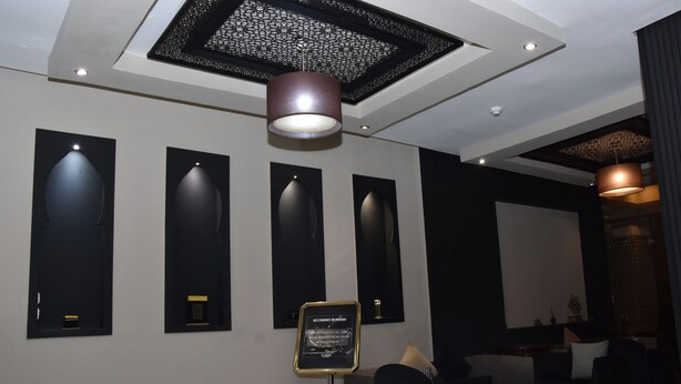 A modern interior with a ceiling design, recessed lighting, and a seating area with tables and chairs. - Cadé Hotel (Casablanca)