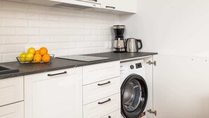 A compact kitchen with white cabinets, a black countertop, a coffee maker, and a washing machine. - Studio with Sea View | Parking | By the Beach (Pobierowo)