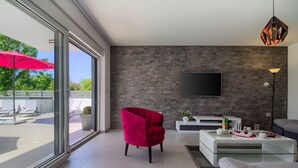 A modern living room with a large TV, a red chair, and a glass coffee table. - Villa Ema with private pool by WiiBuk (Istria - Sisan) (Sisan)