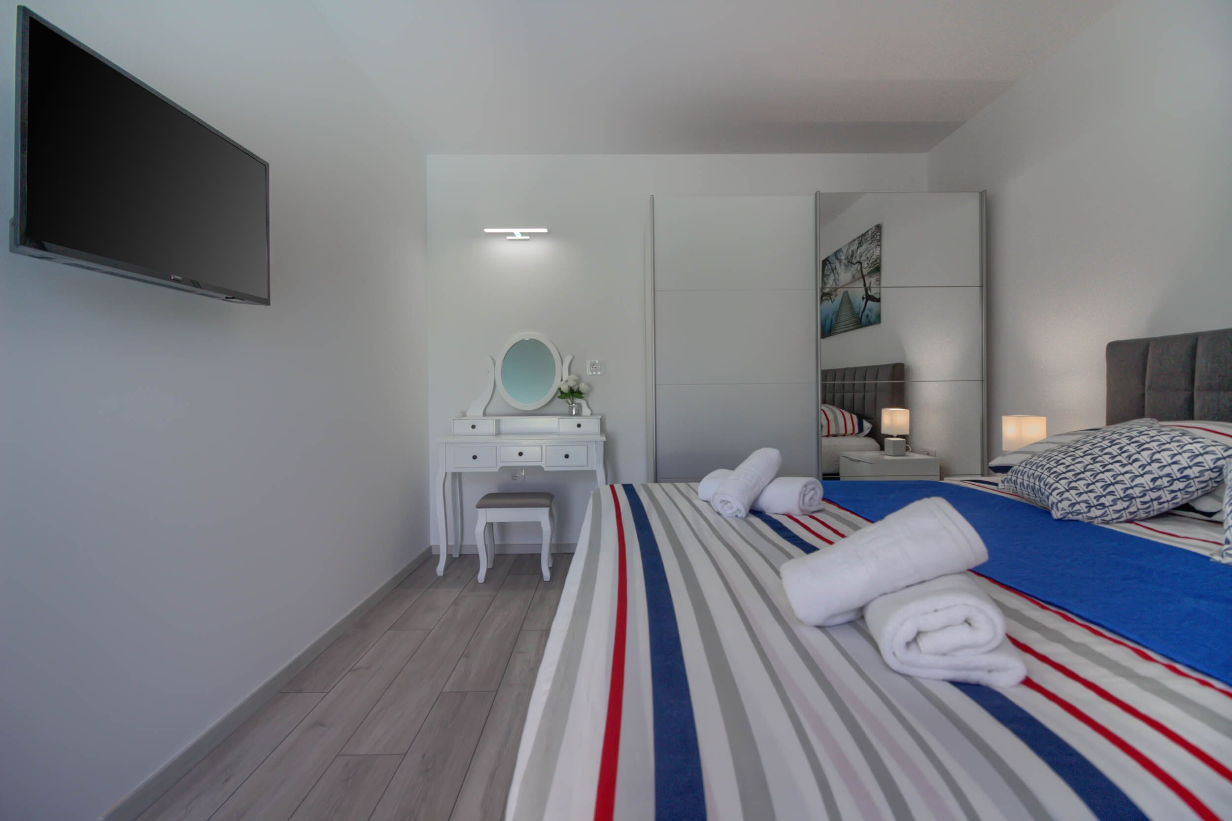 Hotellihuone, jossa on sänky, kirjoituspöytä peilillä, taulutelevisio ja taulu seinällä.