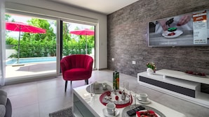 A modern living room with a red chair, a white coffee table, and a TV mounted on a textured wall. - Villa Ema with private pool by WiiBuk (Istria - Sisan) (Sisan)