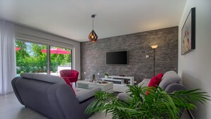 A modern living room with a grey sofa, red armchairs, a coffee table, and a TV mounted on a textured wall. - Villa Ema with private pool by WiiBuk (Istria - Sisan) (Sisan)