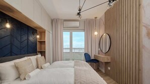 A modern bedroom with a bed, a desk, and a view through a window. - Elegant Apartment | Air Conditioning | Balcony | Workspace. (Wroclaw)