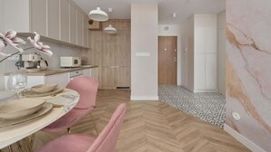 A modern kitchen with wooden cabinets, a dining area with pink chairs, and a marble wall. - Elegant Apartment | Air Conditioning | Balcony | Workspace. (Wroclaw)