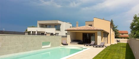 Et moderne hus med swimmingpool, terrasse med liggestole og en velplejet græsplæne.