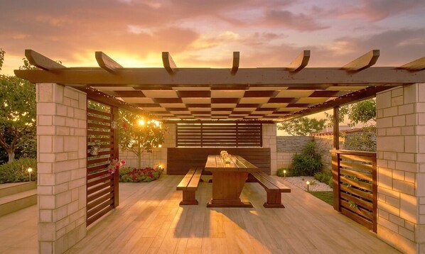 An outdoor patio with a wooden pergola, a central table, and benches.