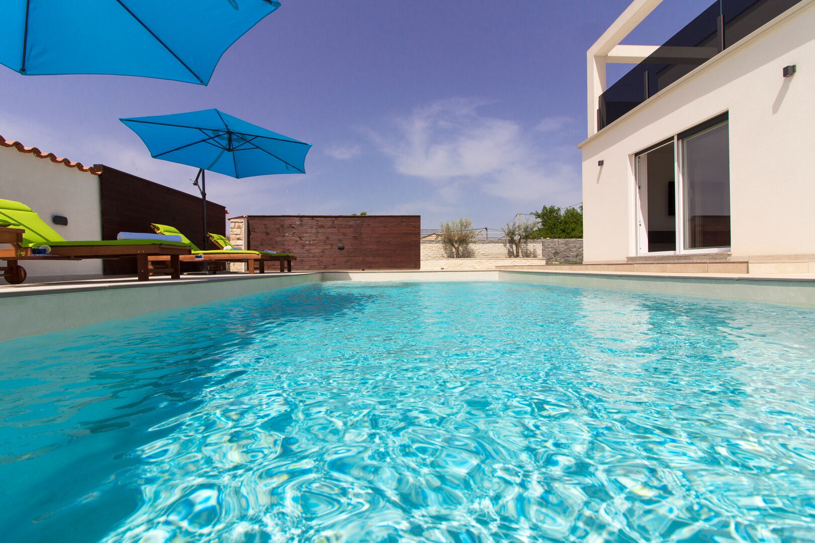 Una piscina cristalina con sillas de descanso y sombrillas, rodeada por un edificio moderno con grandes ventanales.