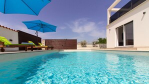 Una piscina limpida con lettini e ombrelloni, circondata da un edificio moderno con ampie finestre.