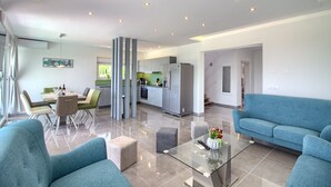 A modern living room with a glass coffee table, two sofas, a dining area with a table and chairs, and a kitchen with a refrigerator and stove. - Villa Horizont (Istria - Fažana) (Fažana)