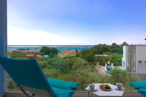 Un balcon avec une table dressée pour le petit-déjeuner, offrant une vue sur une ville côtière et un ciel bleu azur.