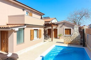 A two-story house with a swimming pool, wooden shutters, and a stone wall.