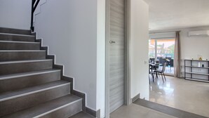 Eine Treppe führt zu einem Raum mit einer Schiebetür, einem Essbereich mit Stühlen und einem Tisch sowie einem Regal mit Gegenständen an der Wand.