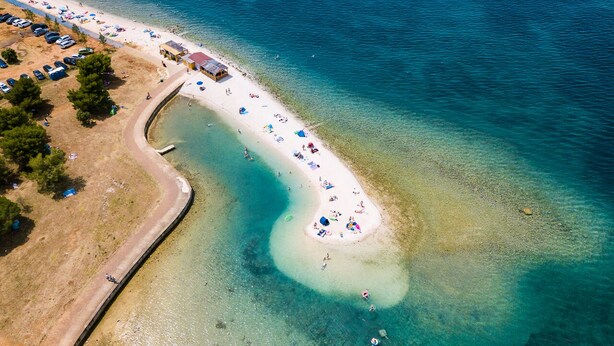 Eine Luftaufnahme eines Strandes mit klarem Wasser, sandigem Ufer und einigen Strandsonnenschirmen.