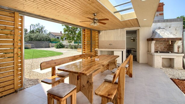 An outdoor patio with a wooden table and benches, a ceiling fan, and a brick barbecue grill. - Villa Antonici (Istria - Liznjan) (Liznjan)
