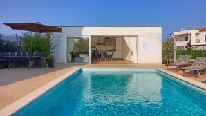 A modern house with a swimming pool, outdoor seating, and a kitchen visible through glass doors. - Villa Rampic (Istria - Fažana) (Fažana)
