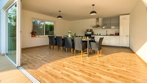 A modern kitchen with a dining area, featuring a large window, a sliding glass door, and a wooden floor. - Villa Rampic (Istria - Fažana) (Fažana)
