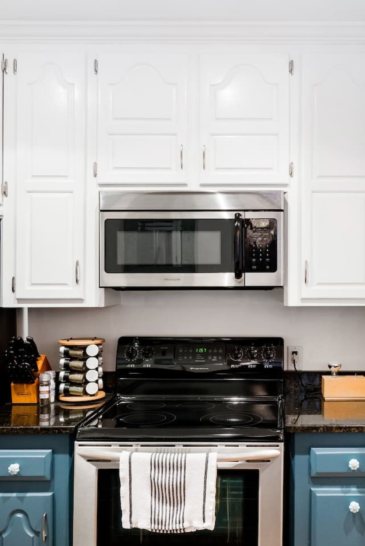 A kitchen with white cabinets, a stainless steel microwave, a black stove, and a blue cabinet.