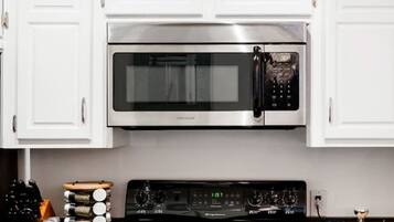 A kitchen with white cabinets, a stainless steel microwave, a black stove, and a blue cabinet.